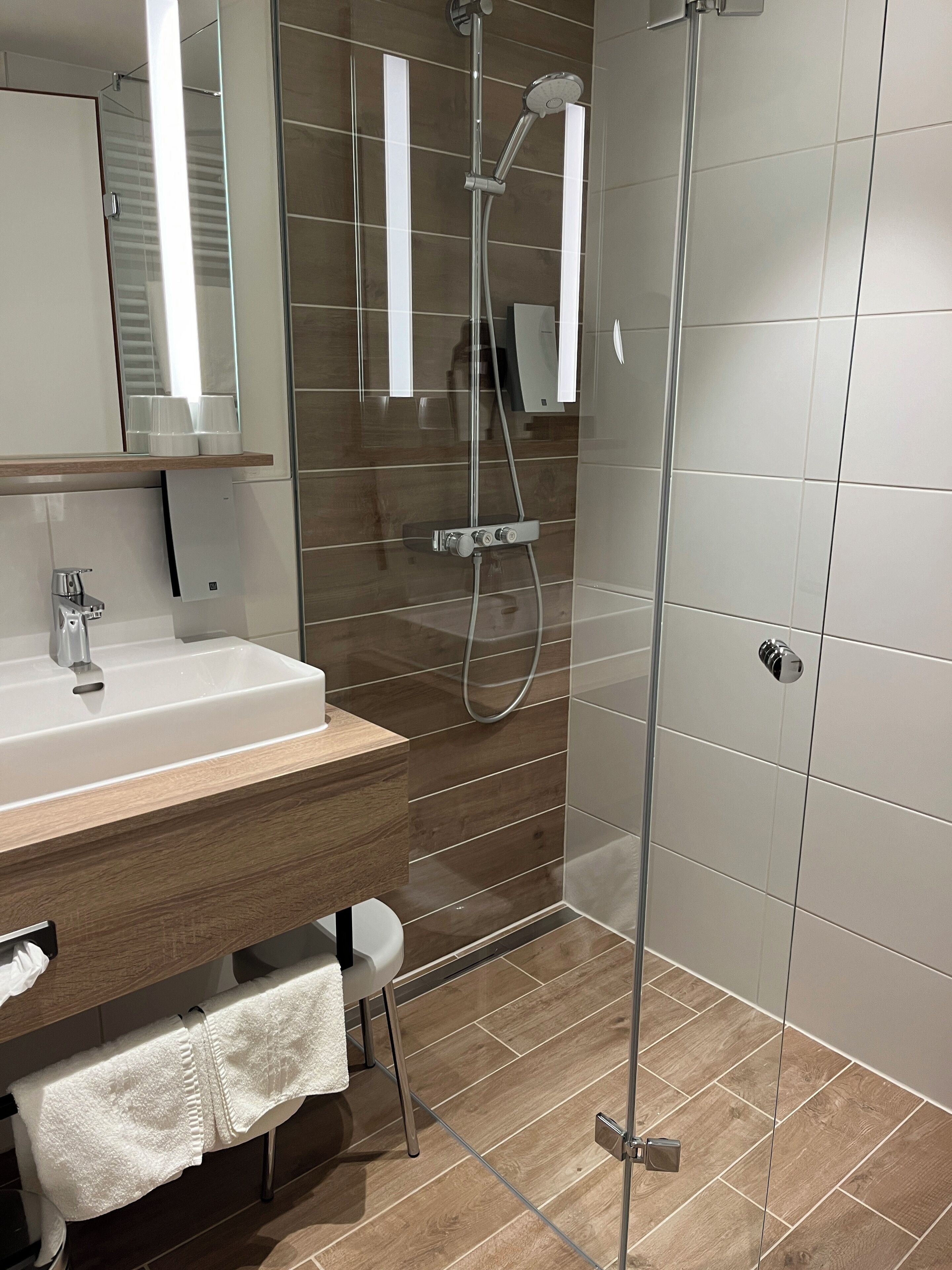 A modern bathroom with a wooden vanity, a glass shower enclosure, and a white sink.