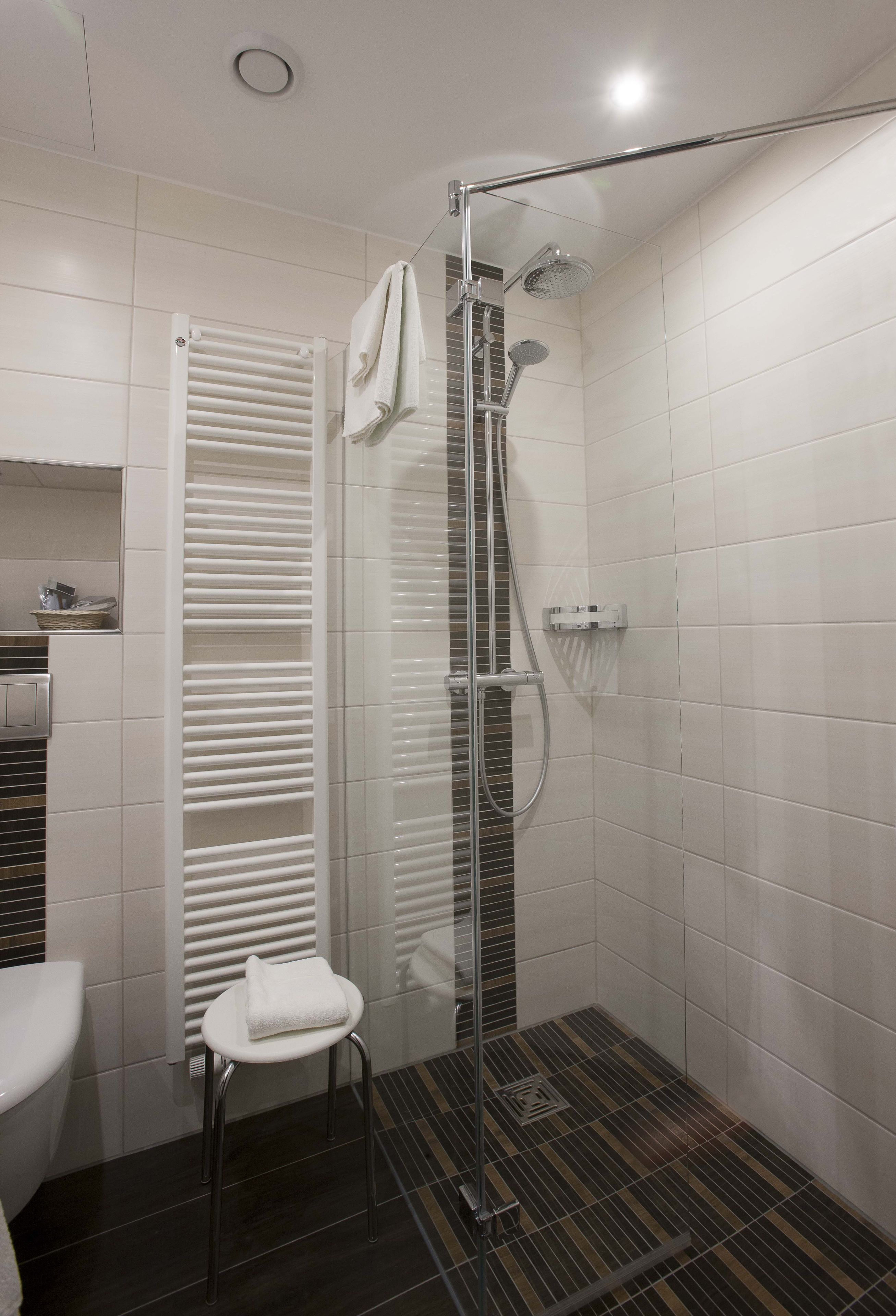 Une salle de bain moderne avec une douche à parois de verre, une serviette blanche posée sur un tabouret et un sol carrelé.