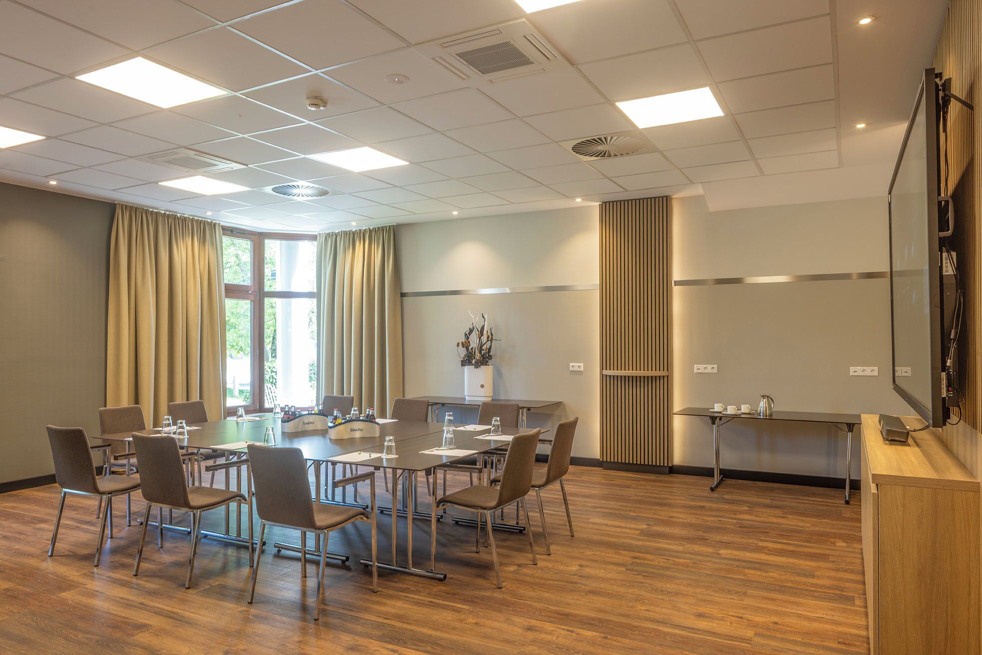 Sala de conferência com uma mesa grande, cadeiras, um espaço para café e uma tela de projeção.