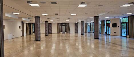 Un amplio y luminoso vestíbulo de hotel, con suelo de madera pulida, altas columnas y grandes ventanales que permiten la entrada de luz natural.
