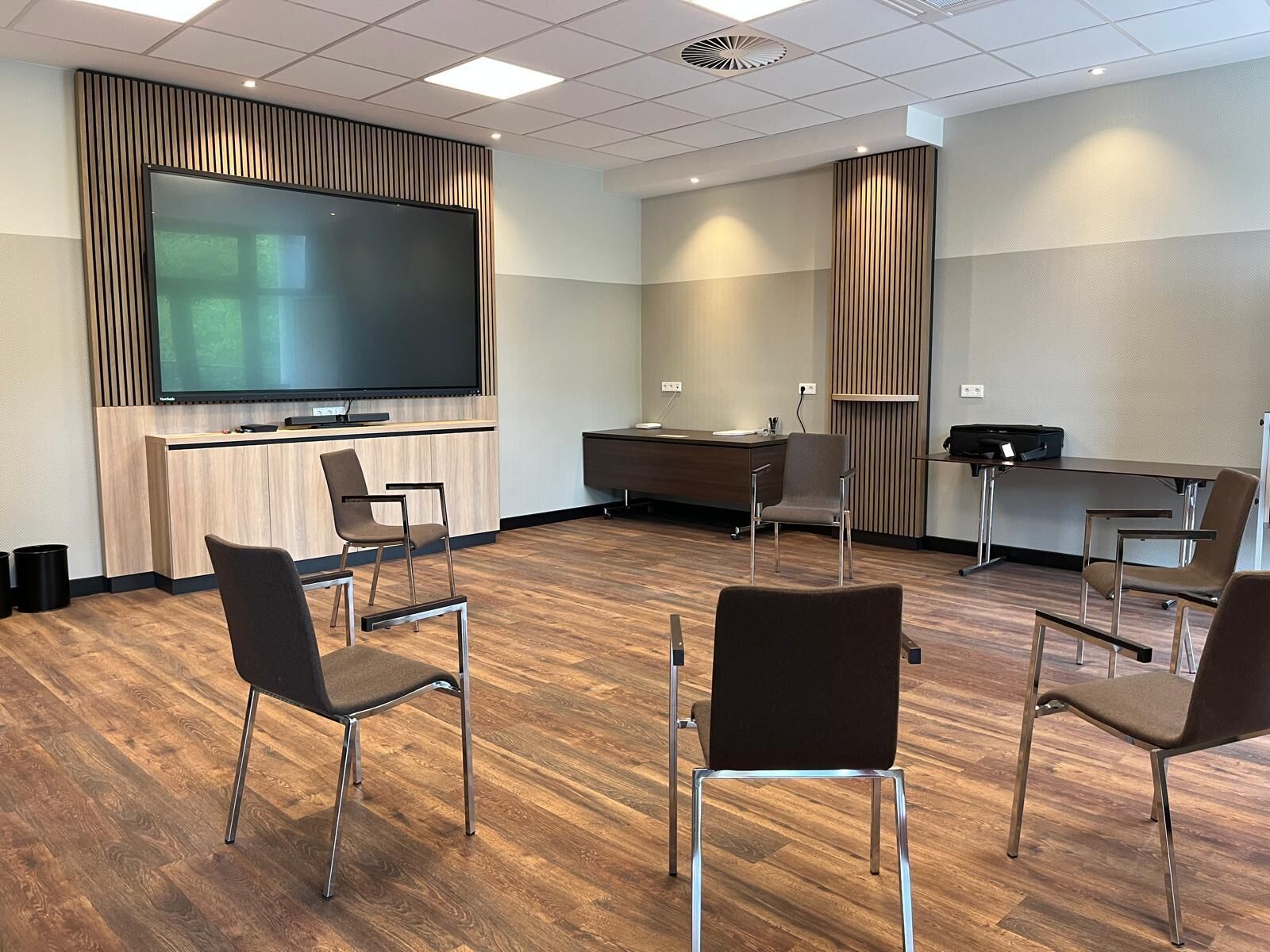 A conference room with a large flat-screen TV, a wooden desk, and several chairs.
