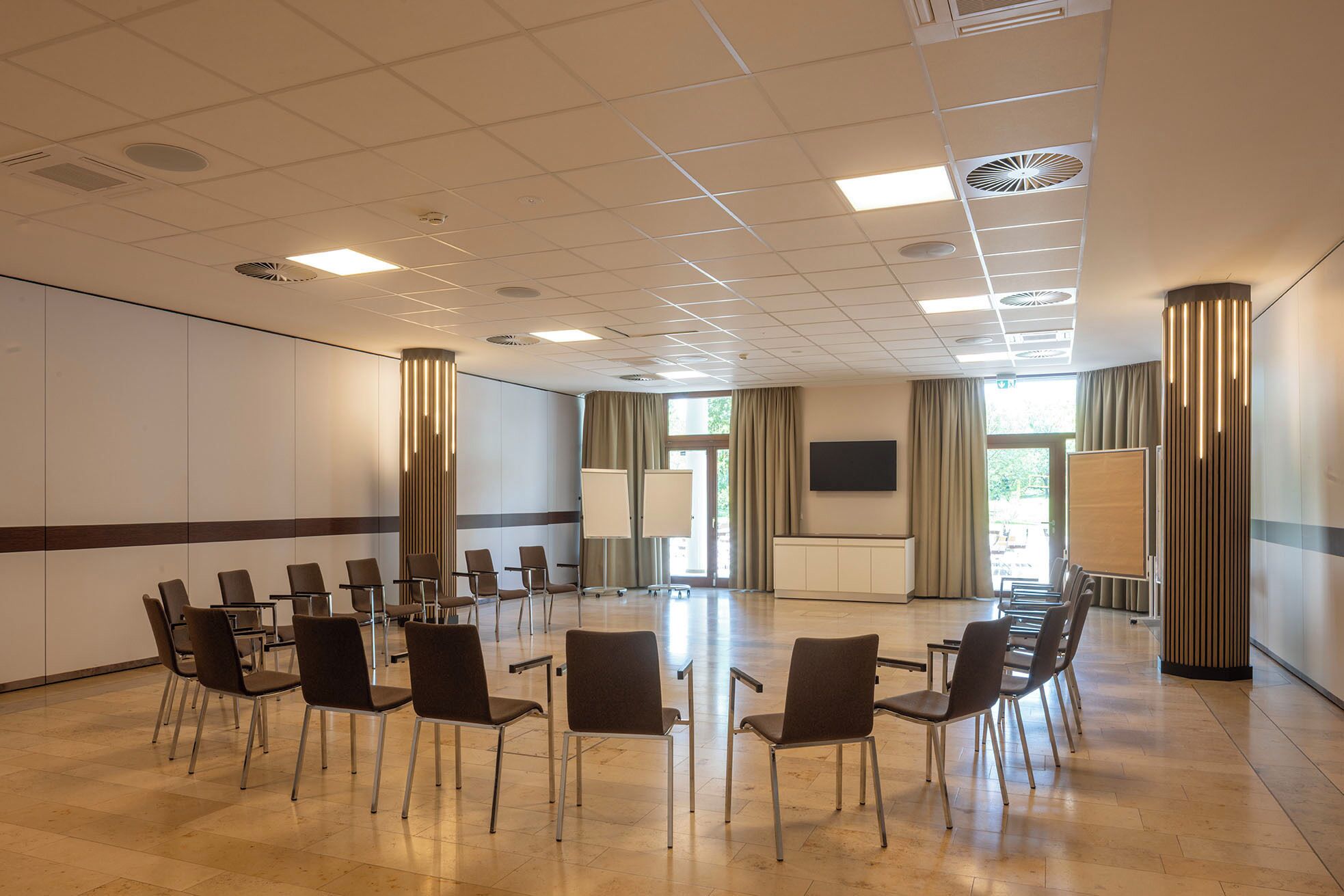 A conference room with a large table and chairs, a TV screen, and a view of the outdoors through the windows.