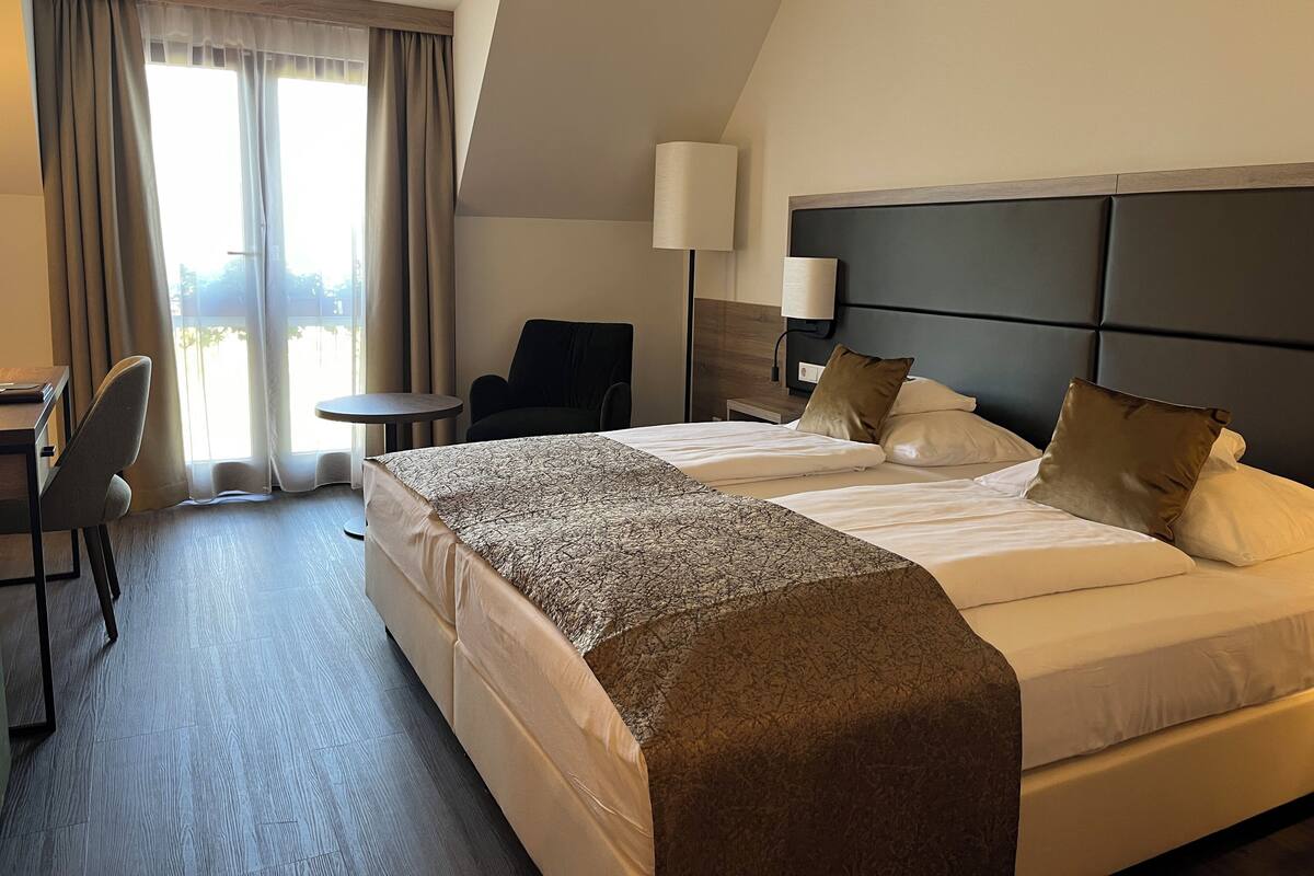A hotel room with two beds, a desk, a chair, a lamp, and a view of the outdoors.