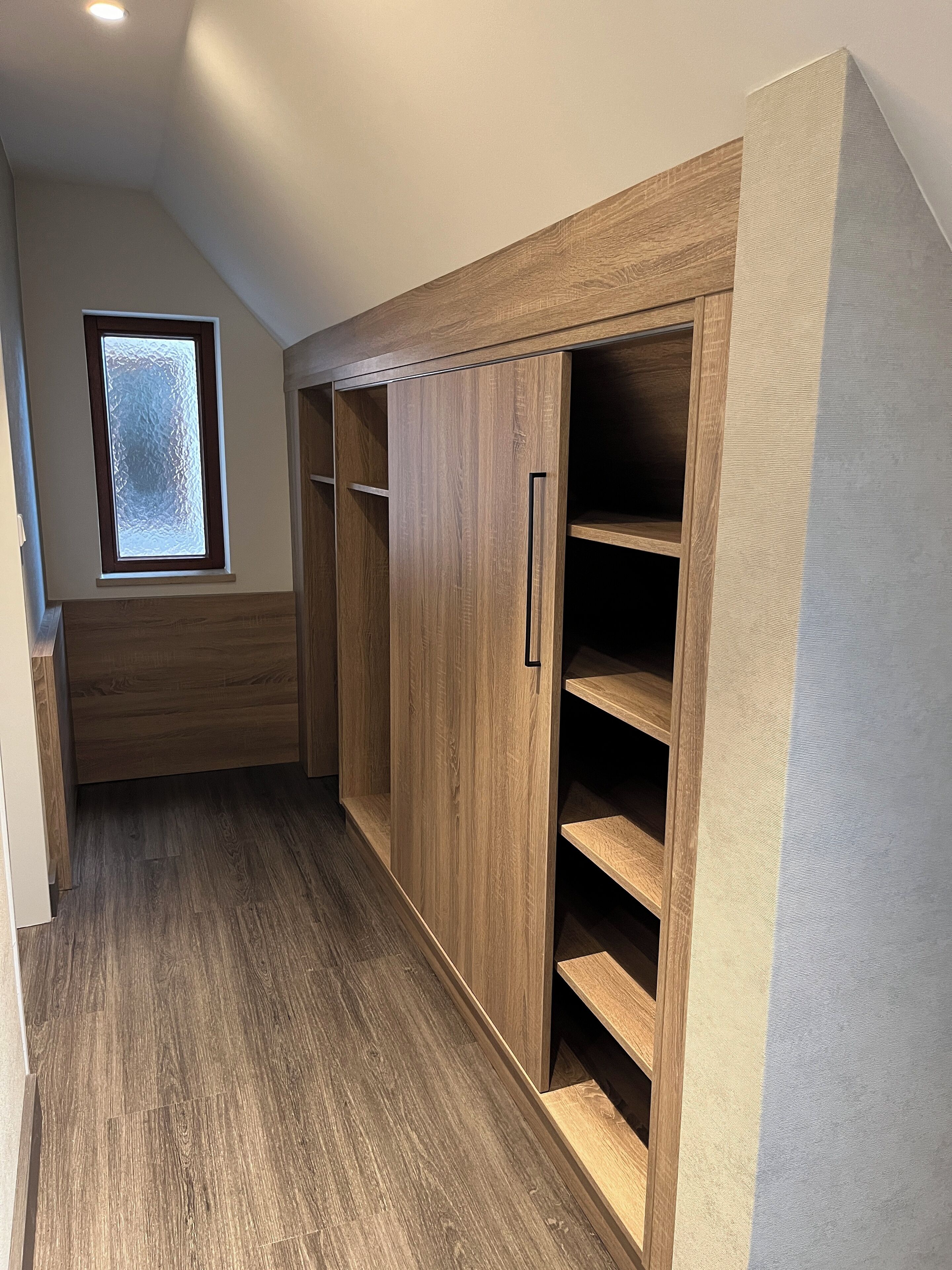 A room with a wooden wardrobe, a small window, and a sloped ceiling.