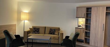 A modern living room with a sofa, two armchairs, a coffee table, and a built-in wooden shelving unit.