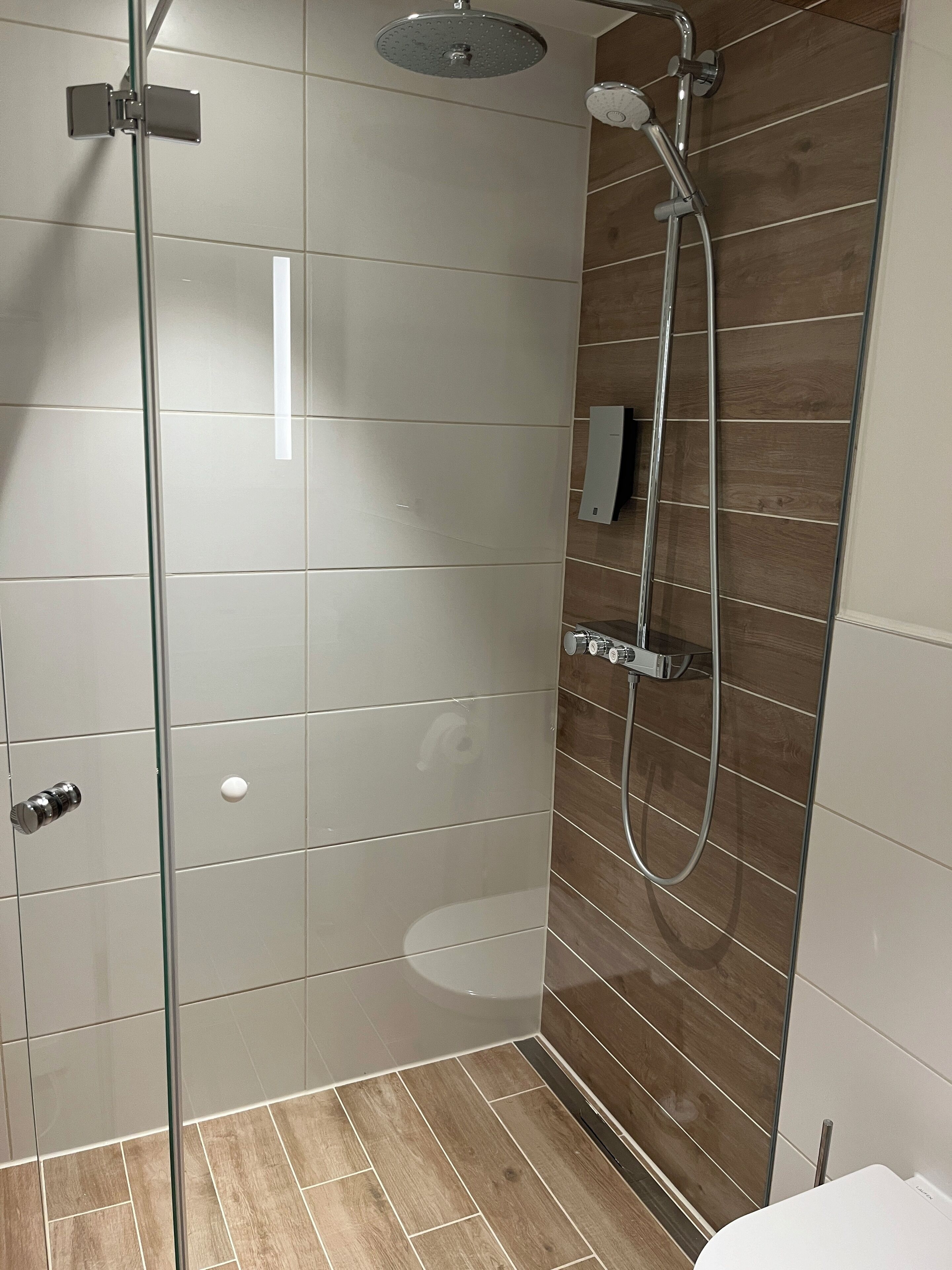 A modern shower with a glass door, a wooden panel wall, and a tiled floor.