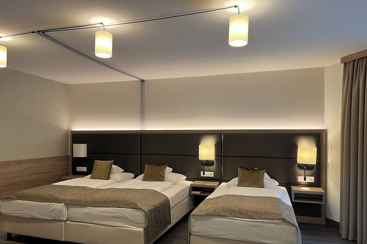 A hotel room with two beds, a headboard, bedside lamps, and a window with curtains.