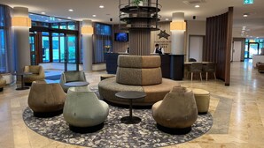 Un moderno vestíbulo de hotel con una zona de estar central, una recepción y un amplio ventanal con vistas al exterior.