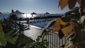 A pool area with umbrellas and a view of the sea. - Aronis Apartments (Corfu)