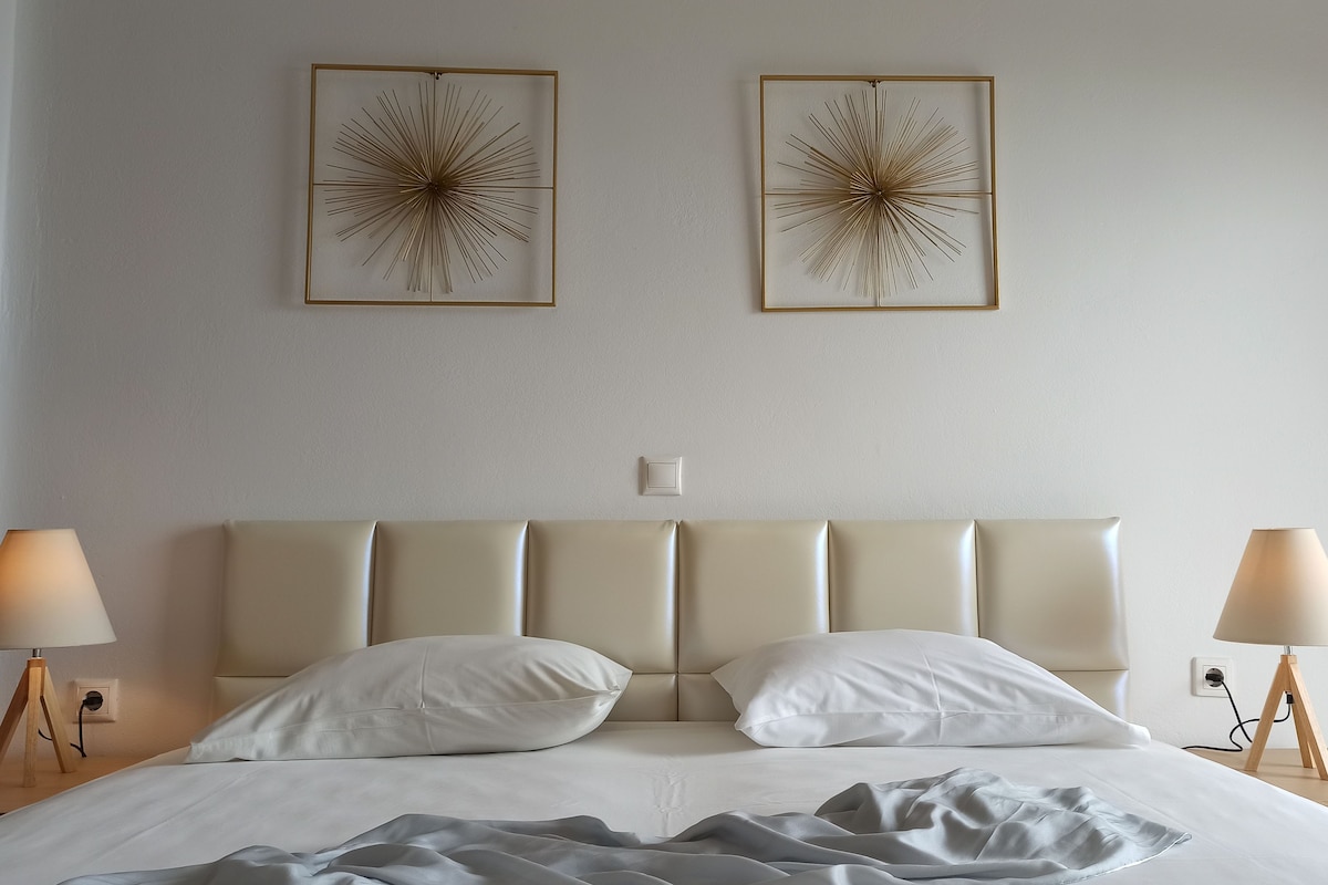 A neatly made bed with two pillows, a bedside lamp on each side, and two wall-mounted abstract art pieces.