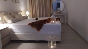 A bedroom with a bed, bedside table, lamp, and a mirror on a dresser. - Aronis Apartments (Corfu)