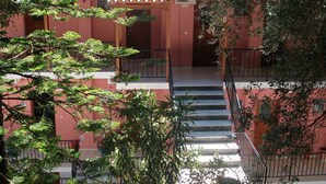A multi-story building with a red facade, a tiled roof, and a staircase leading to the upper floor. - Aronis Apartments (Corfu)