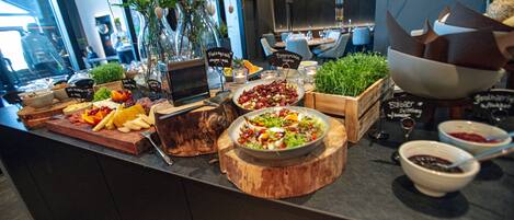 A buffet with various food items and a wooden cutting board.
