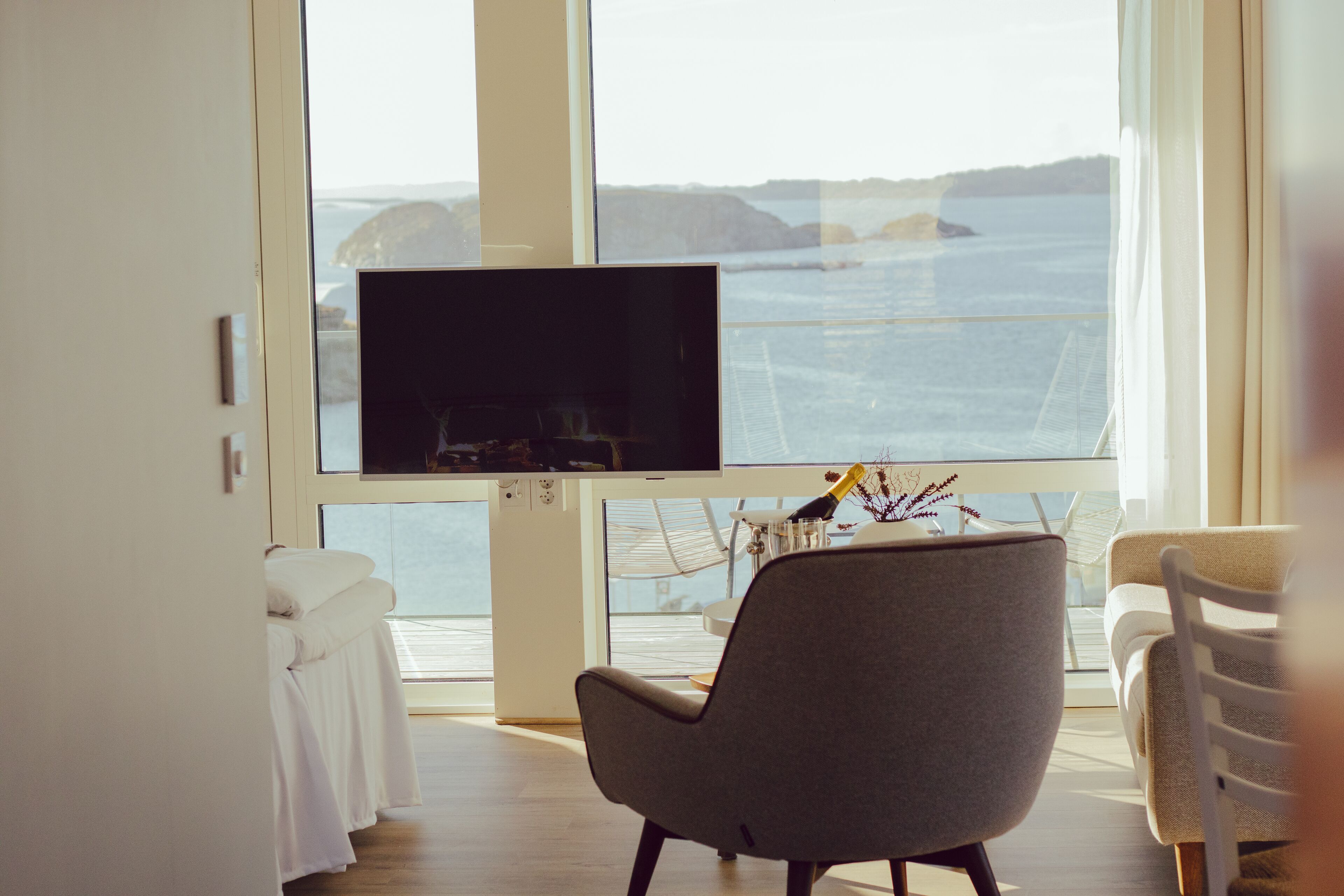 Una habitación moderna con un televisor grande en la pared, un sillón gris cómodo y vistas al mar a través de amplios ventanales.