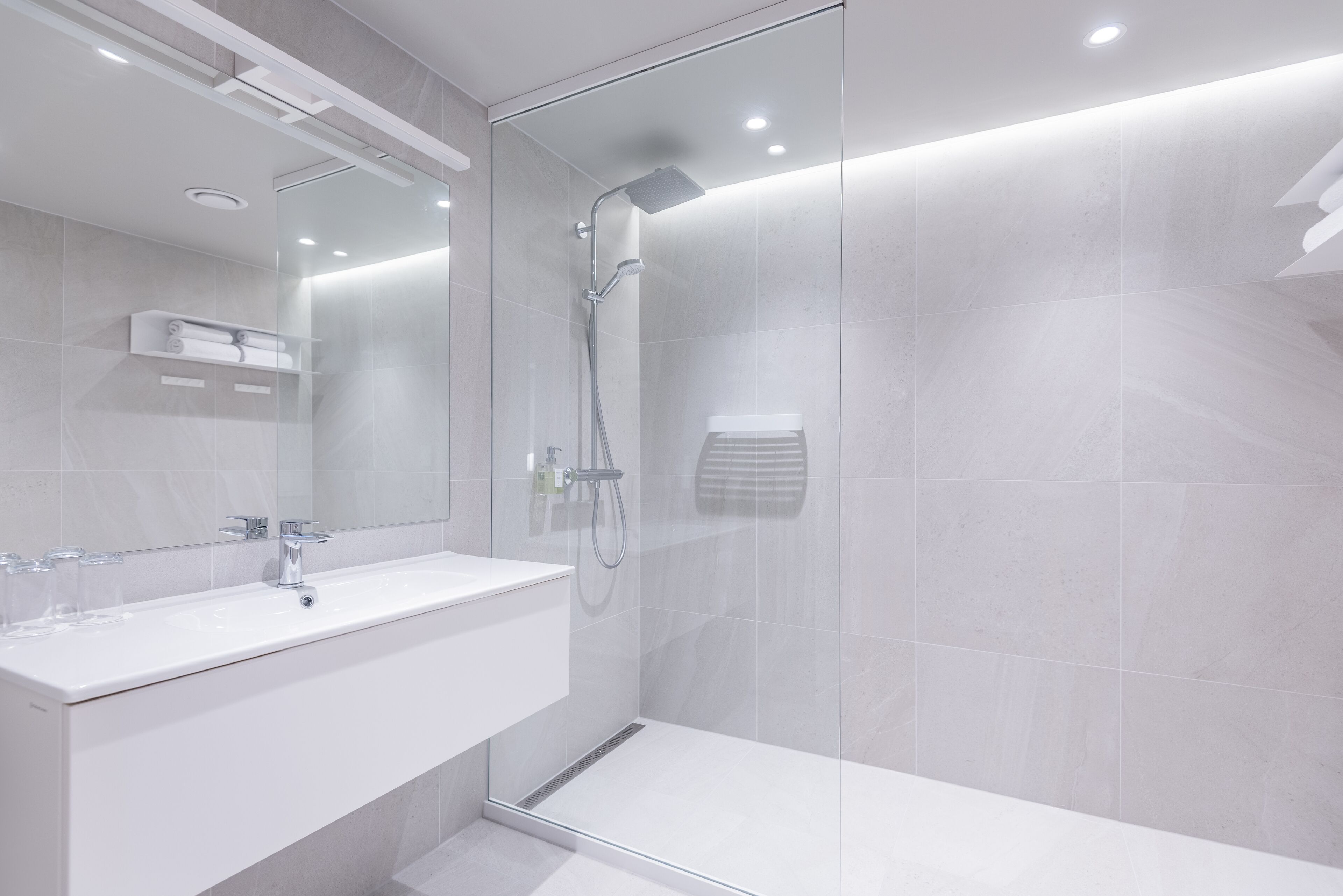A modern bathroom with a glass-enclosed shower, a white sink, and a large mirror.