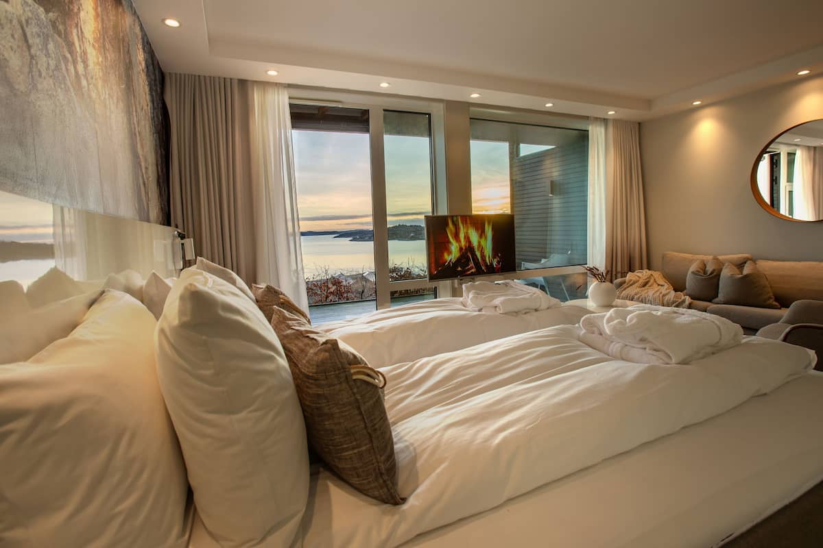 A modern hotel room with a large bed, a sofa, and a TV displaying a fire.