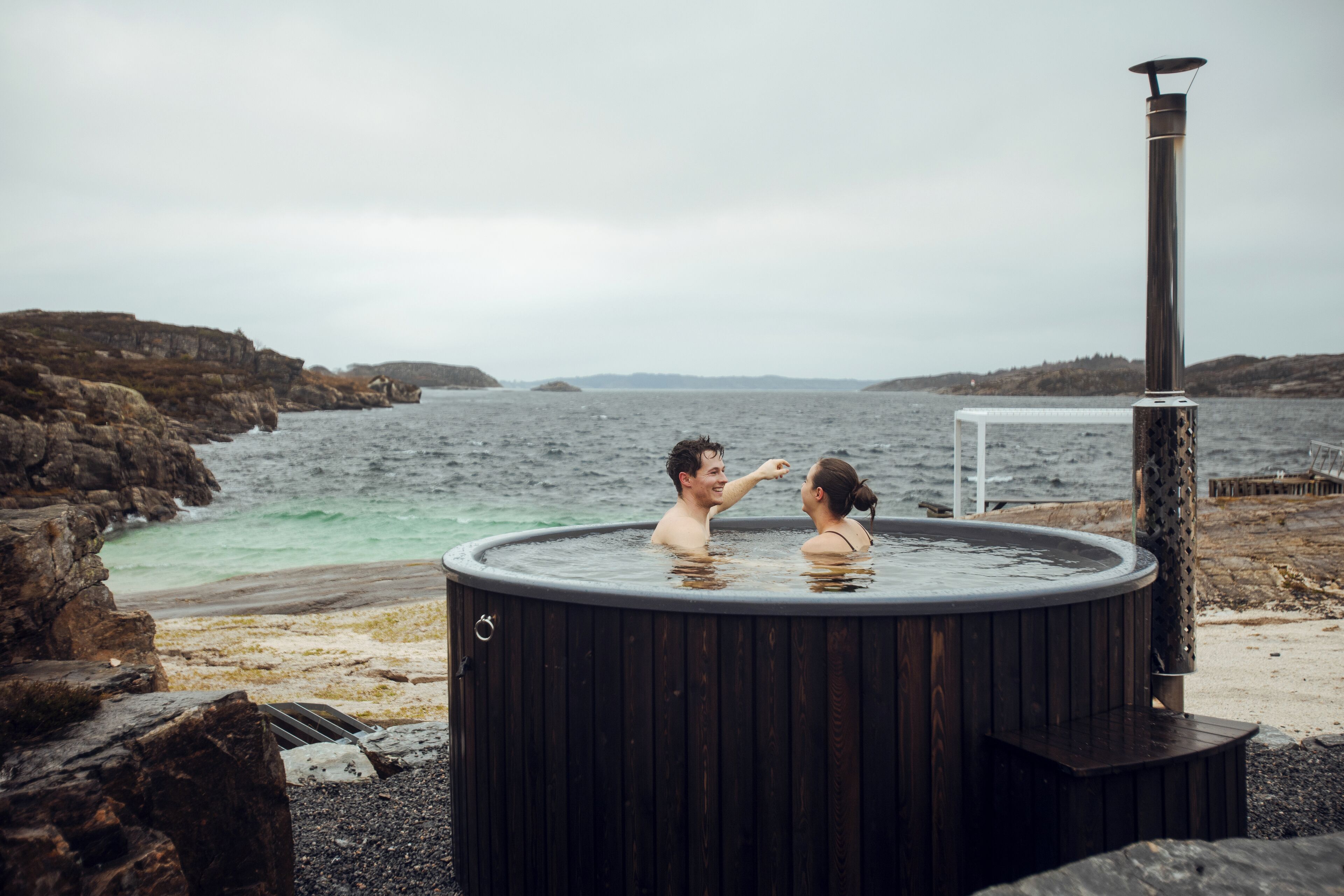 A hot tub with a chimney, located by a rocky shoreline with a view of the sea.