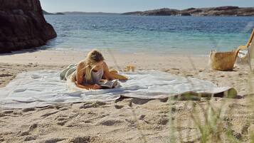 A person reading on a beach towel with a rocky cliff and calm sea in the background.