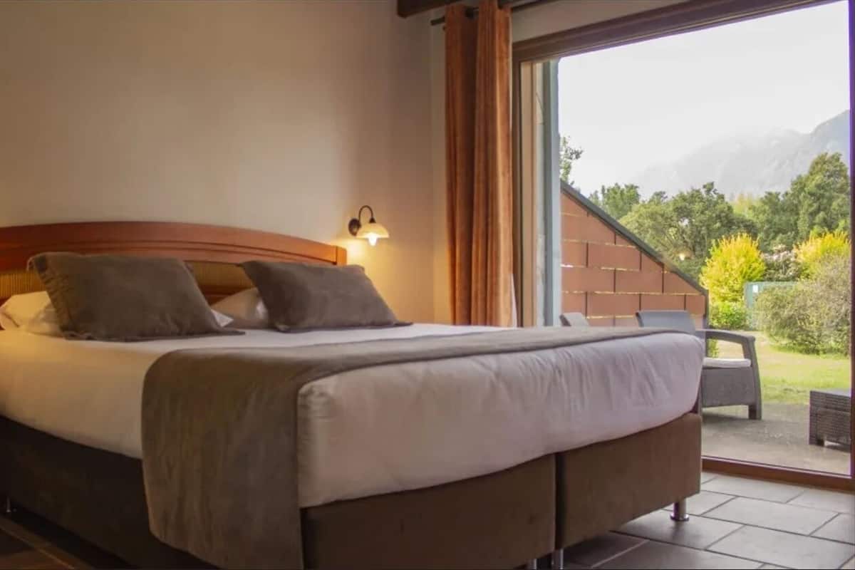 Ein Bett mit Kopfteil, zwei Nachttischlampen und Blick auf einen Balkon mit Gartenmöbeln.
