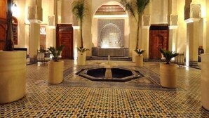 Um hall com piso estampado, uma fonte central e colunas.