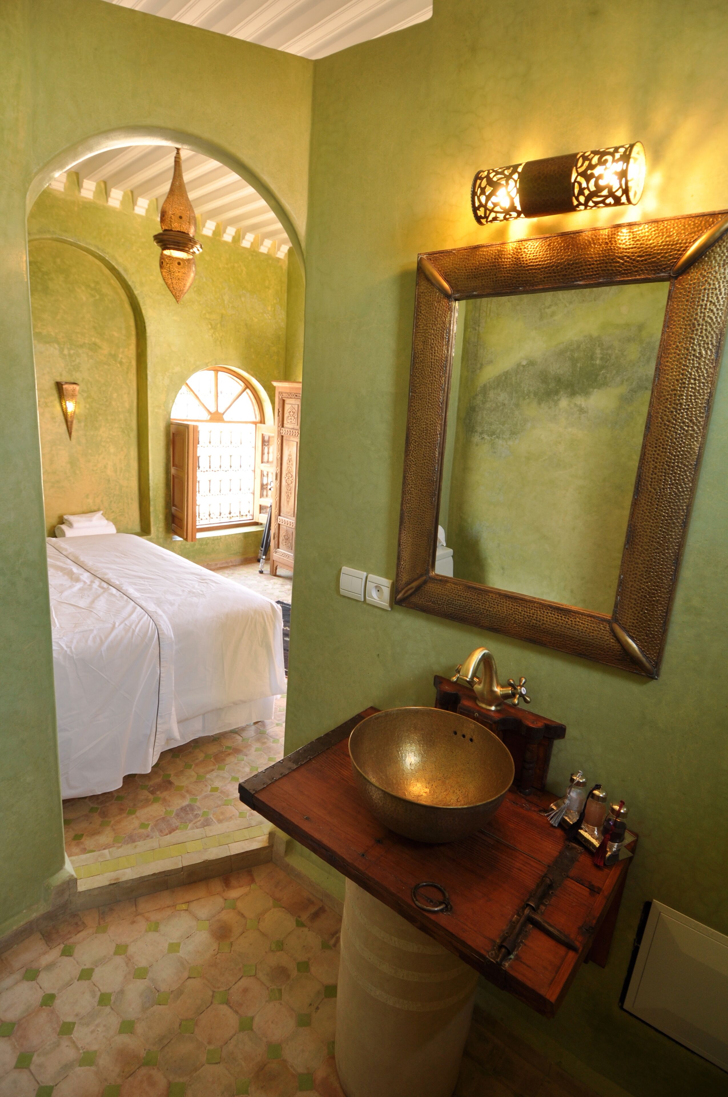 Quarto com cama, pia com cuba grande, espelho e luminária sobre o espelho.