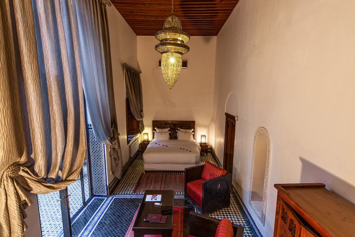 A room with a checkered floor, a bed with red pillows, a wooden ceiling, and a chandelier.