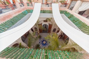 Um pátio em vários níveis com telhados em azulejos verdes, cortinas brancas e uma fonte central.