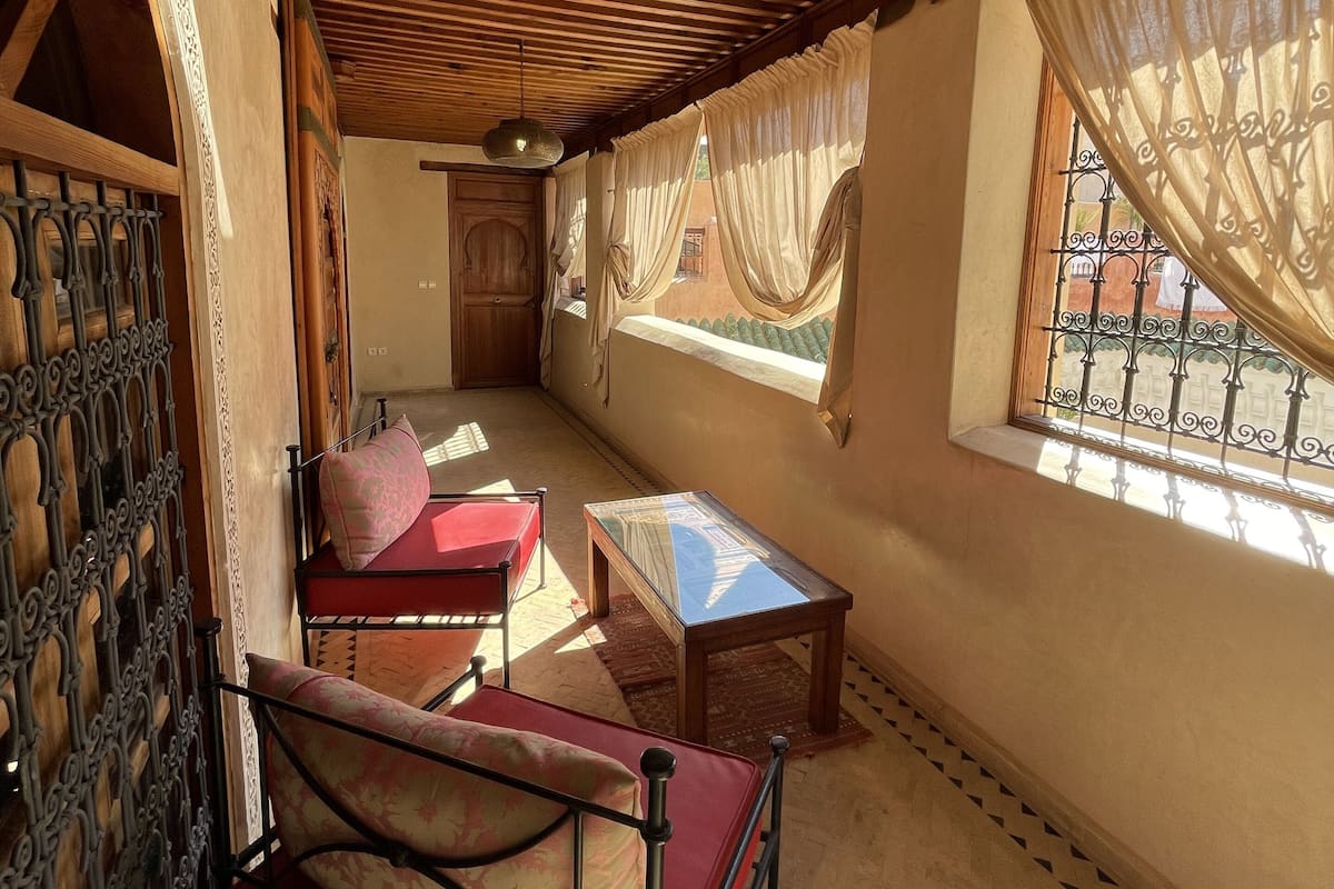 A cozy room with a wooden ceiling, a red sofa, a small table, and a window with curtains.