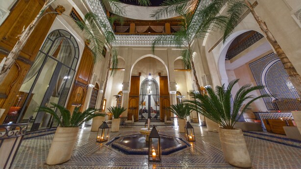 Um lobby luxuoso com uma fonte central, arcos ornamentados e plantas em vasos.