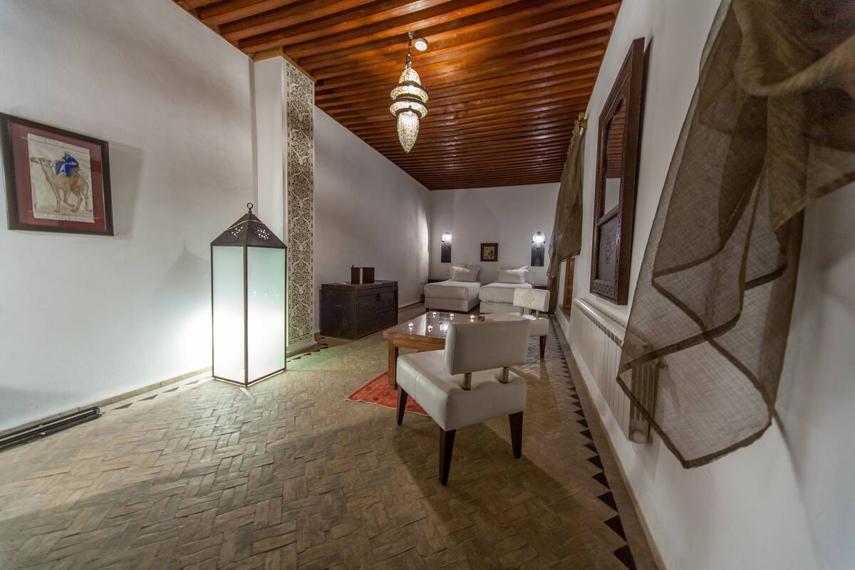 A cozy room with a wooden ceiling, a chandelier, a white sofa set, a small table, and a decorative lantern.