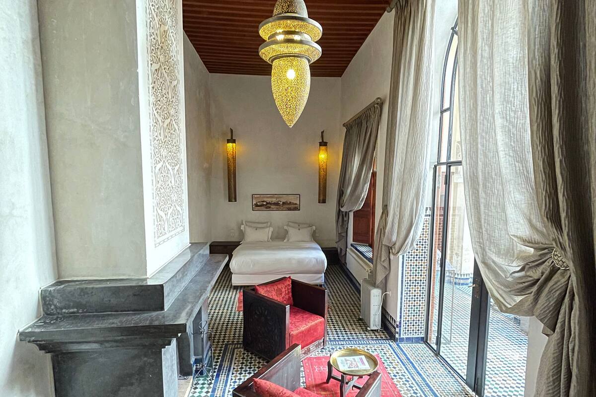 A hotel room with a checkered floor, a bed, a red sofa, a small table, and a chandelier.