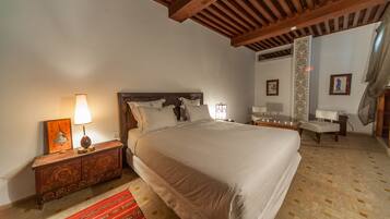 A bedroom with a large bed, wooden headboard, bedside tables with lamps, a red patterned rug, and a decorative wall panel.