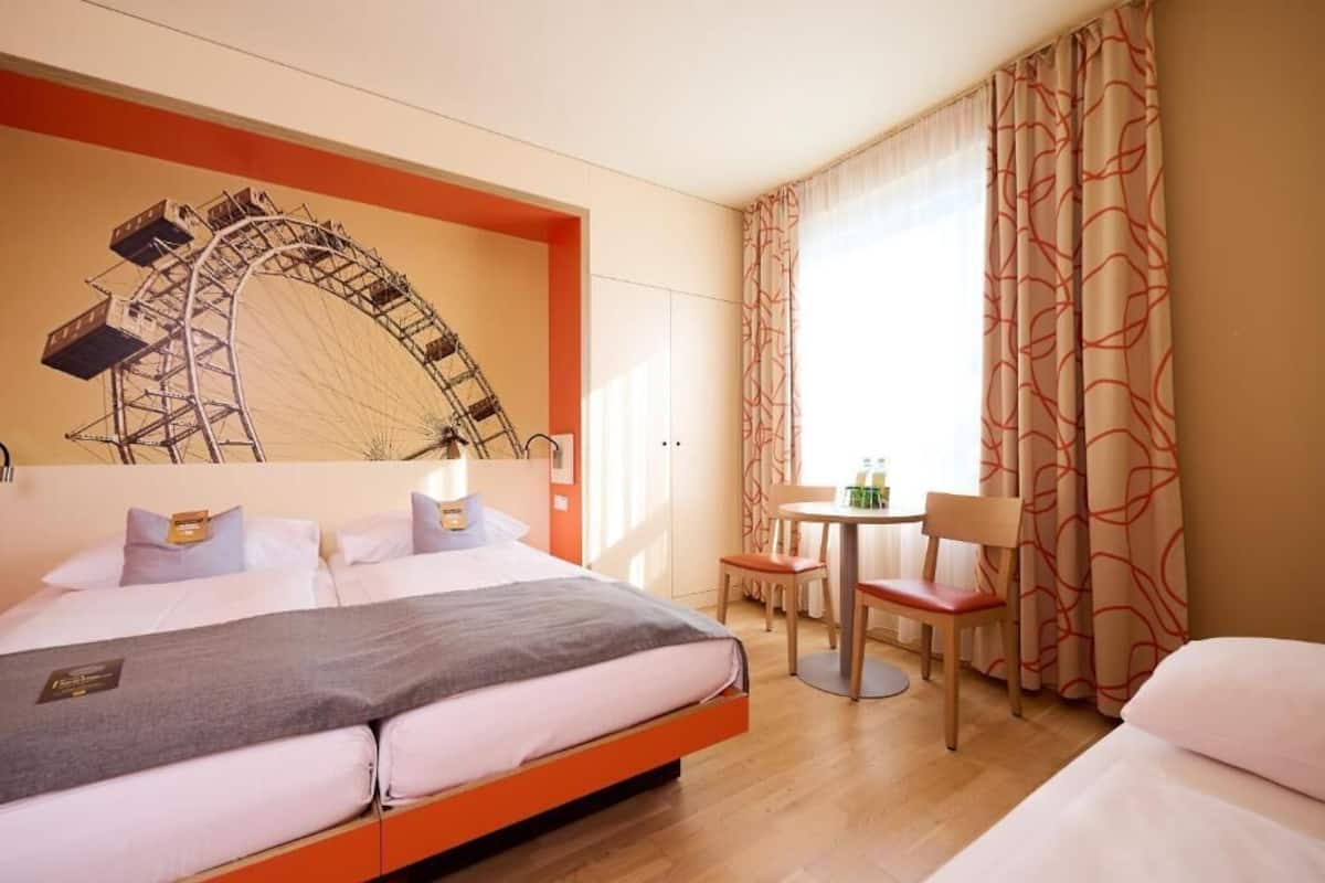 Een hotelkamer met een bed, bureau, stoel en een groot raam met gordijnen.