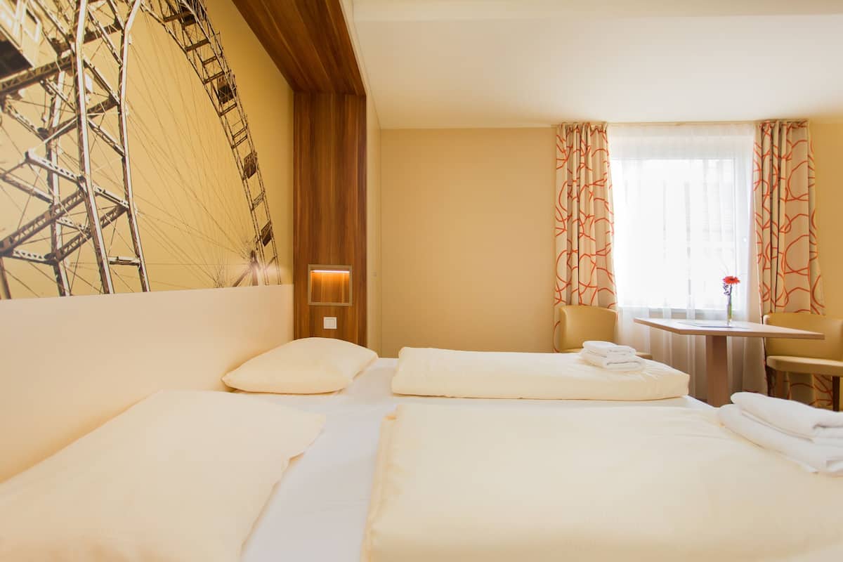 Hotelkamer met twee bedden, een bureau, een stoel, een raam met gordijnen en een wanddecoratie.