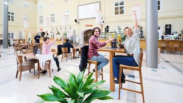 Ein großzügiger Innenbereich mit mehreren Holztischen und Stühlen, einer Lounge und einem großen Bildschirm.