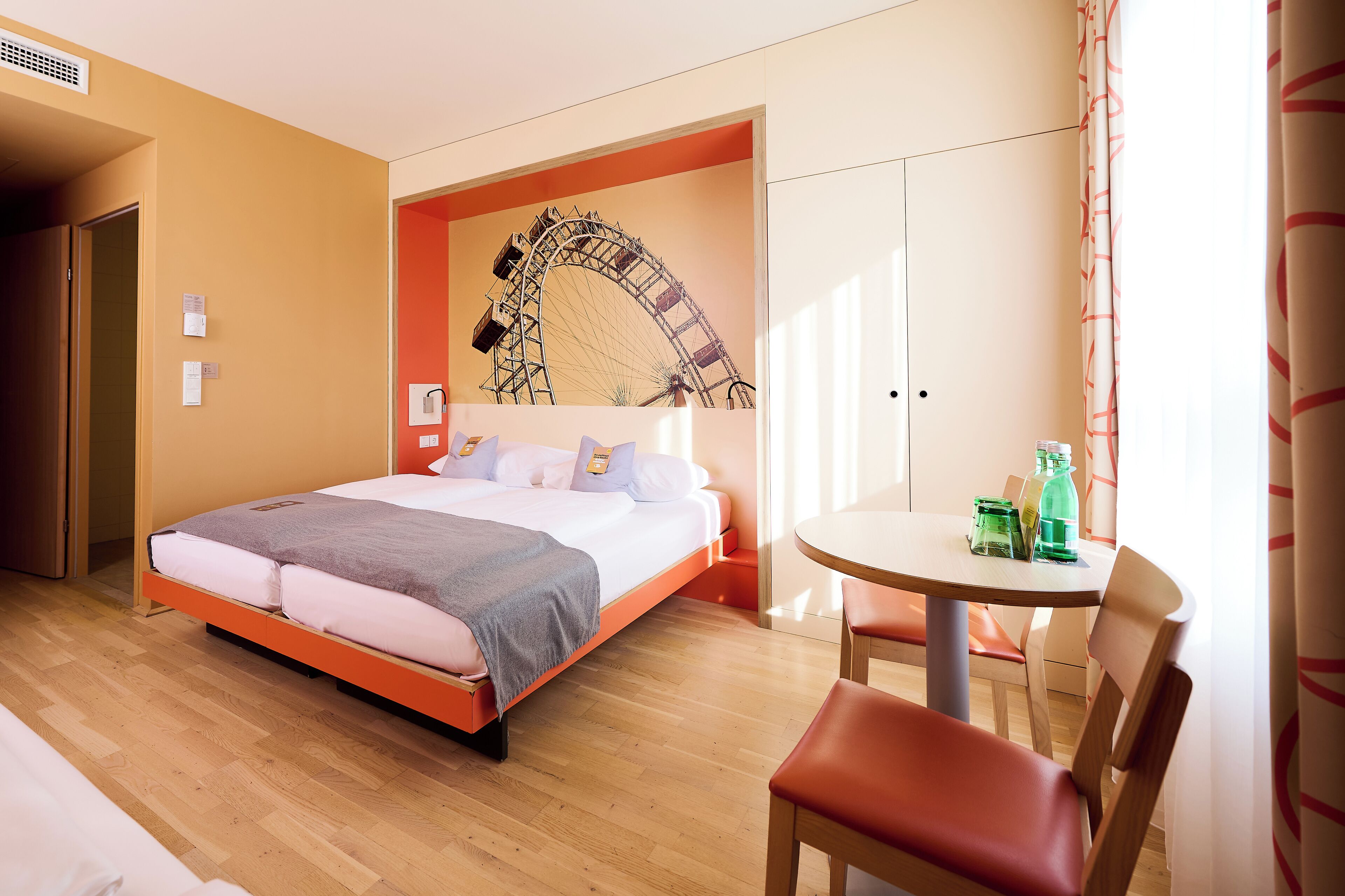 A hotel room with a bed, a table with chairs, and a large window.