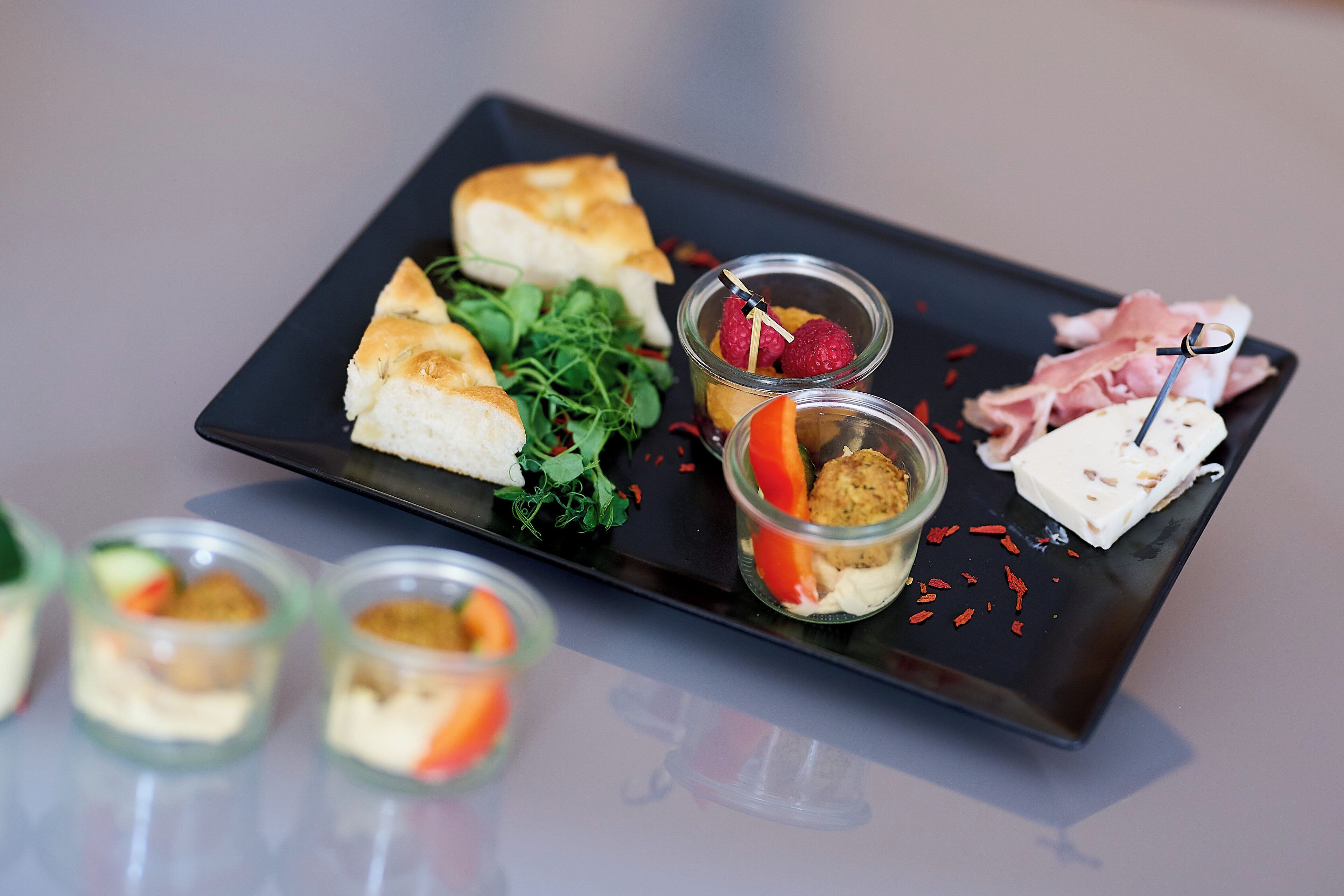 A black rectangular plate with various food items including bread, greens, and small containers with food.