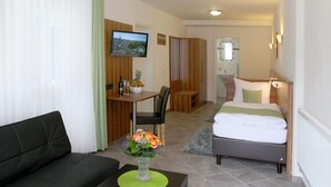 Quarto de hotel com cama, sofá, área de refeições com mesa e cadeiras, televisão e banheiro com espelho.