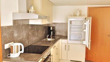 Eine kompakte Küche mit Backofen, Kaffeemaschine und Kühlschrank mit Gefrierfach.