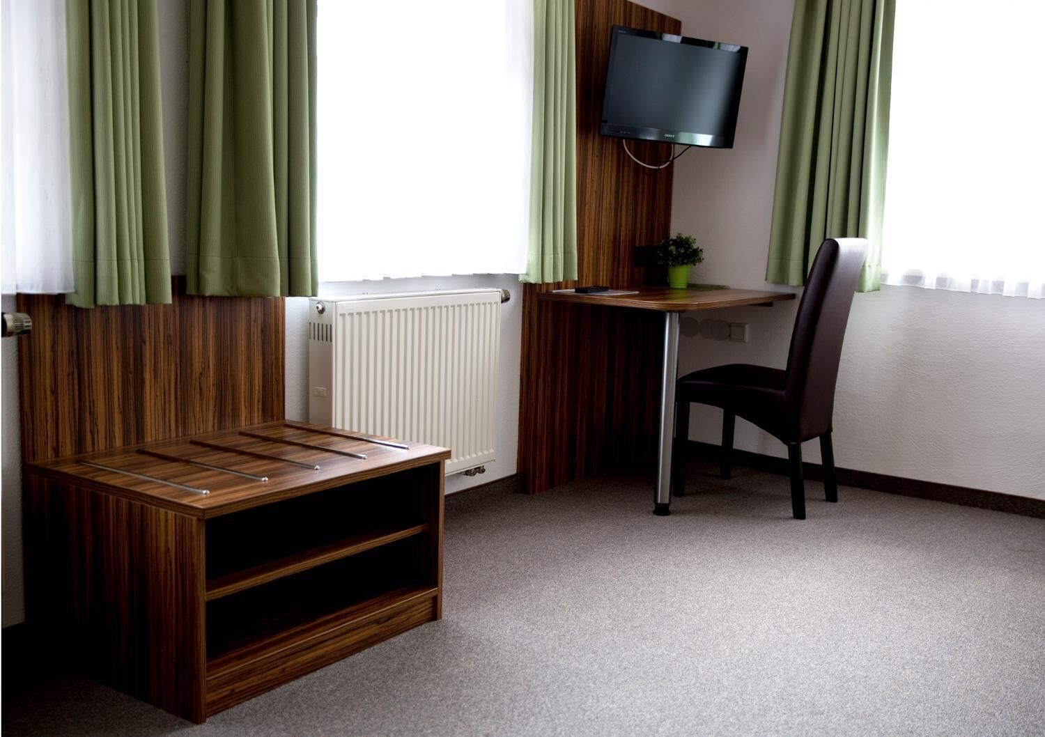 Ein Zimmer mit einem Holztisch, einem Stuhl, einem an der Wand befestigten Fernseher und einer Heizung.