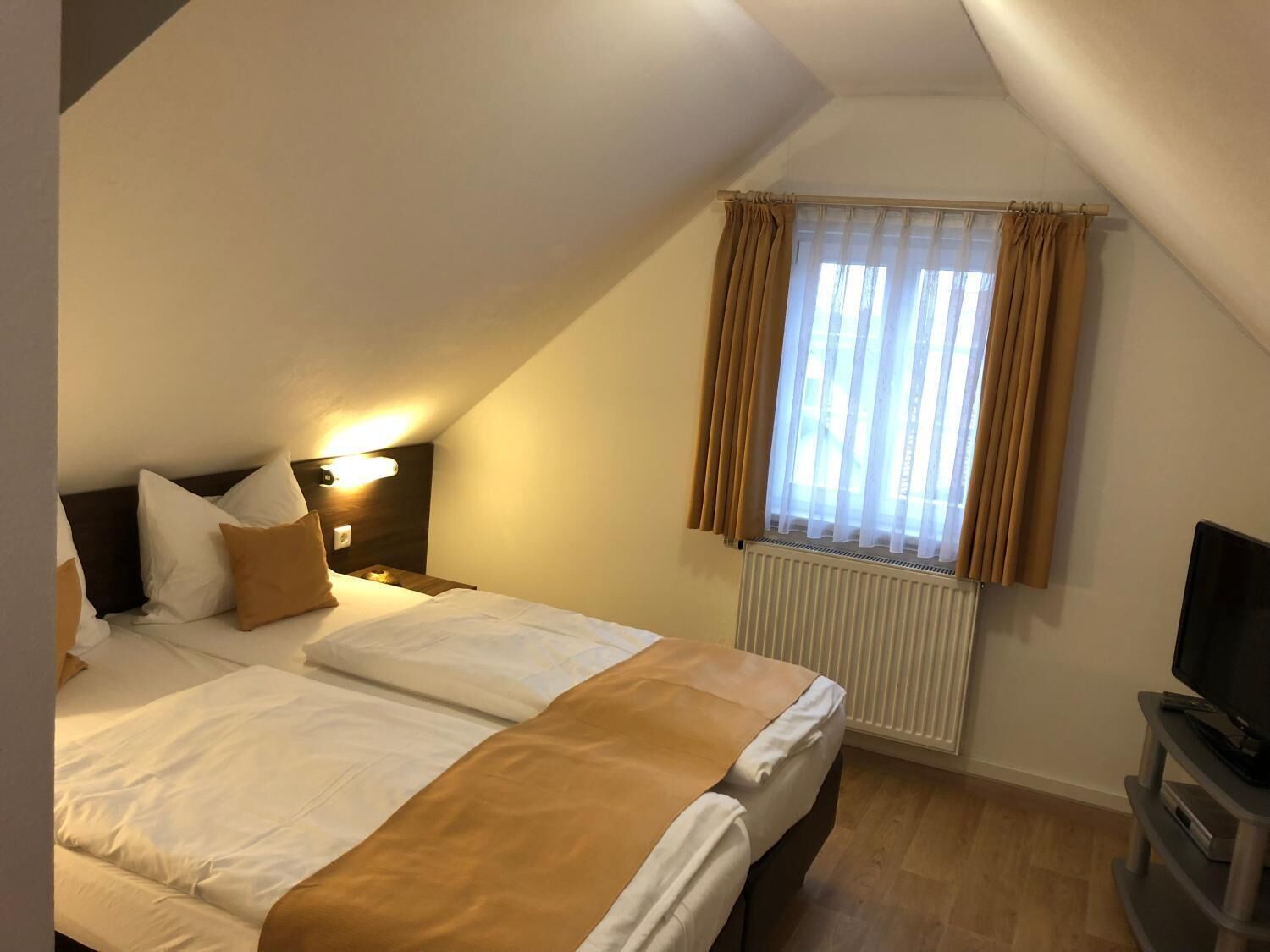 Una habitación de hotel con cama, televisor, ventana con cortinas y radiador.