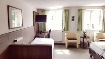 A hotel room with a bed, a desk, a chair, a TV, and a window with curtains.