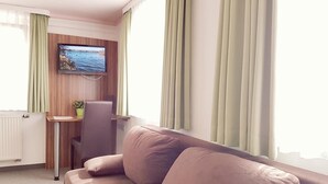 Uma sala de estar moderna com um sofá bege, uma escrivaninha de madeira e uma televisão na parede.