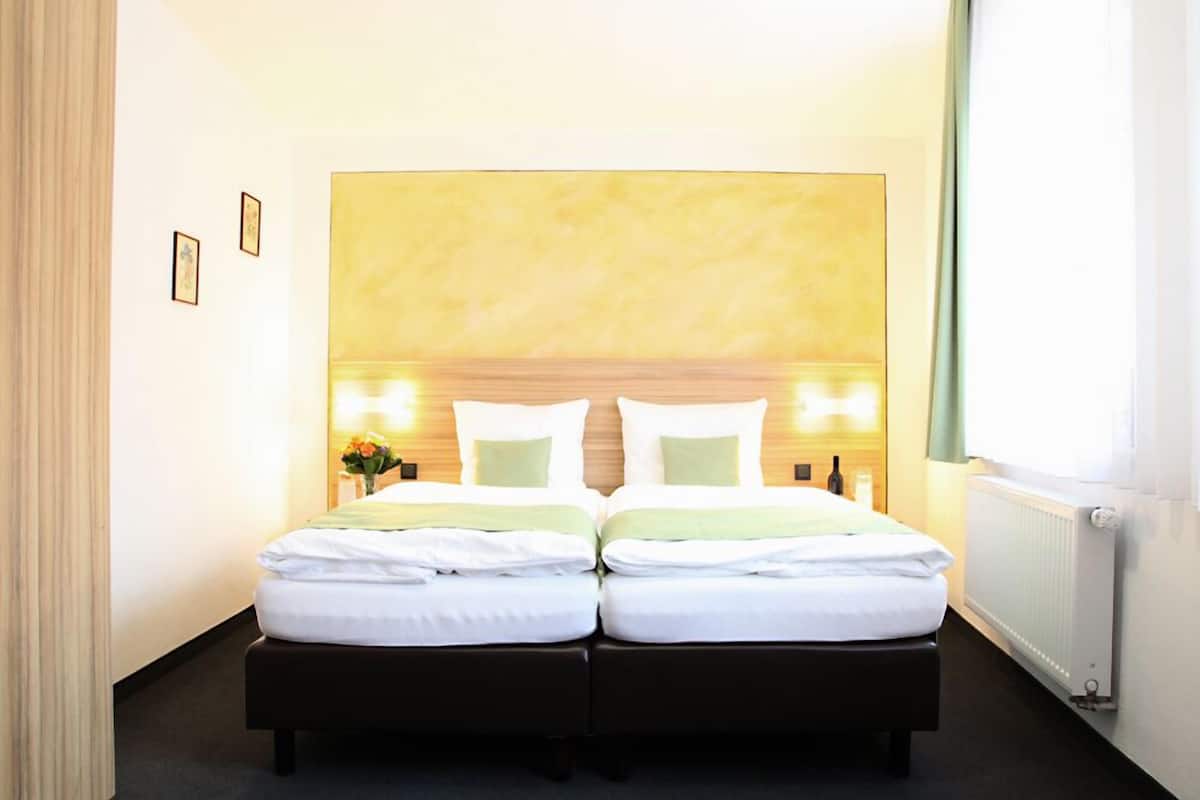 A double bed with white linens, a wooden headboard, bedside lamps, and a vase with flowers.