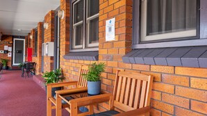A brick building with wooden benches and potted plants. - Port Macquarie Motel (Port Macquarie)