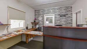 A reception desk with a stone wall backdrop, a clock, and a window with blinds. - Port Macquarie Motel (Port Macquarie)