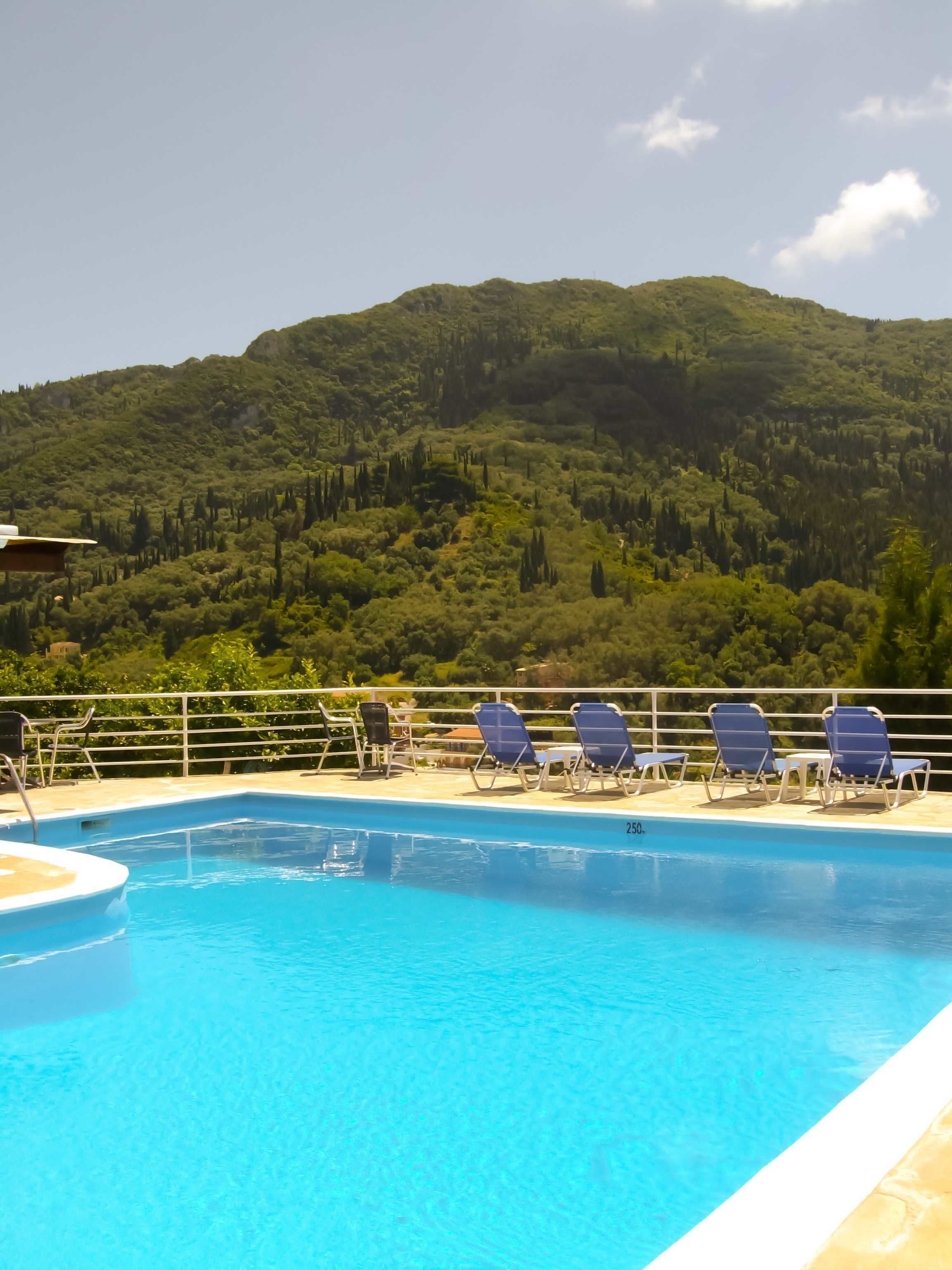 A swimming pool with lounge chairs and a view of a forested hillside.