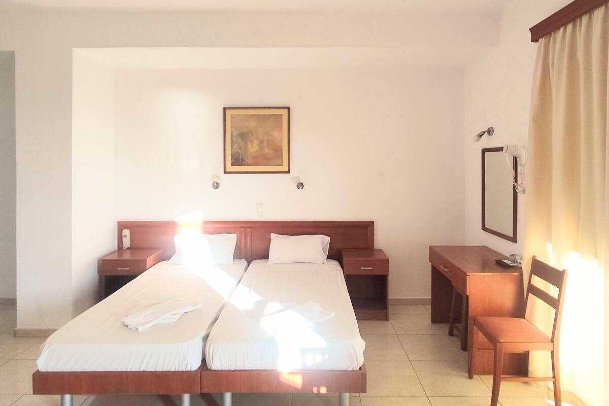 A hotel room with a large bed, a desk, a chair, a bedside table, a mirror, and a painting on the wall.