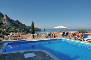 A pool area with lounge chairs and tables, overlooking a scenic mountain and sea view. - Panorama apartments (Corfu)