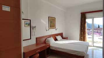 Habitación de hotel con cama, escritorio y silla. Se observa una ventana con cortinas, un cuadro en la pared y una puerta.